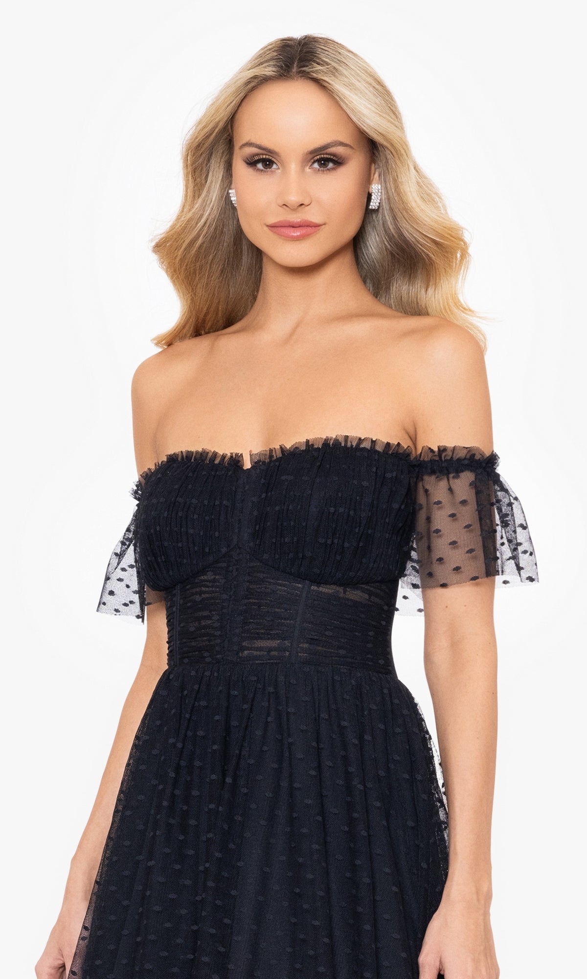 A woman with long blonde hair wears the Swiss Dot Long Black Lace-Up Prom Dress 4601BN, featuring off-the-shoulder sheer short sleeves, while posing against a plain white background.